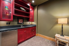 A kitchen with red cabinets, a stainless steel refrigerator, a sink, and a small table with a lamp. - Exclusive Deer Valley 5BR | Hot Tub, Game Room, Views & Ski Shuttle (Park City)