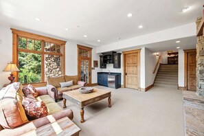 Ein geräumiger Wohnbereich mit einer Couch, einem Couchtisch und Blick ins Freie durch große Fenster.