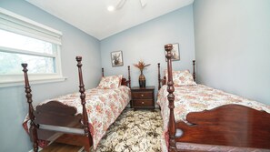 A bedroom with two wooden beds, a nightstand, a vase with dried flowers, and a window with blinds. - 4-bedroom house in delightful North Chicago with AC (North Chicago)