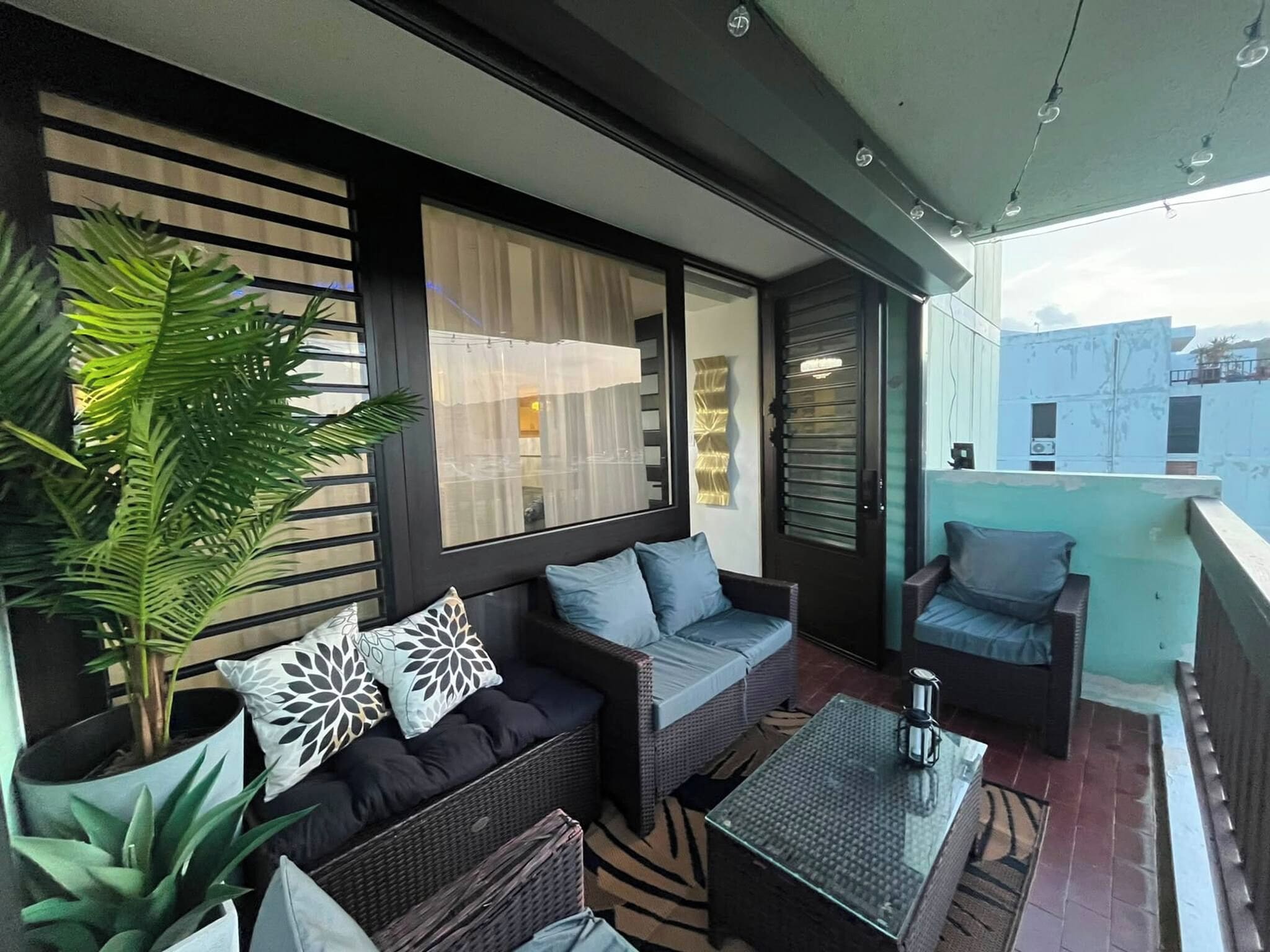 A balcony with wicker furniture, a glass table, and potted plants.