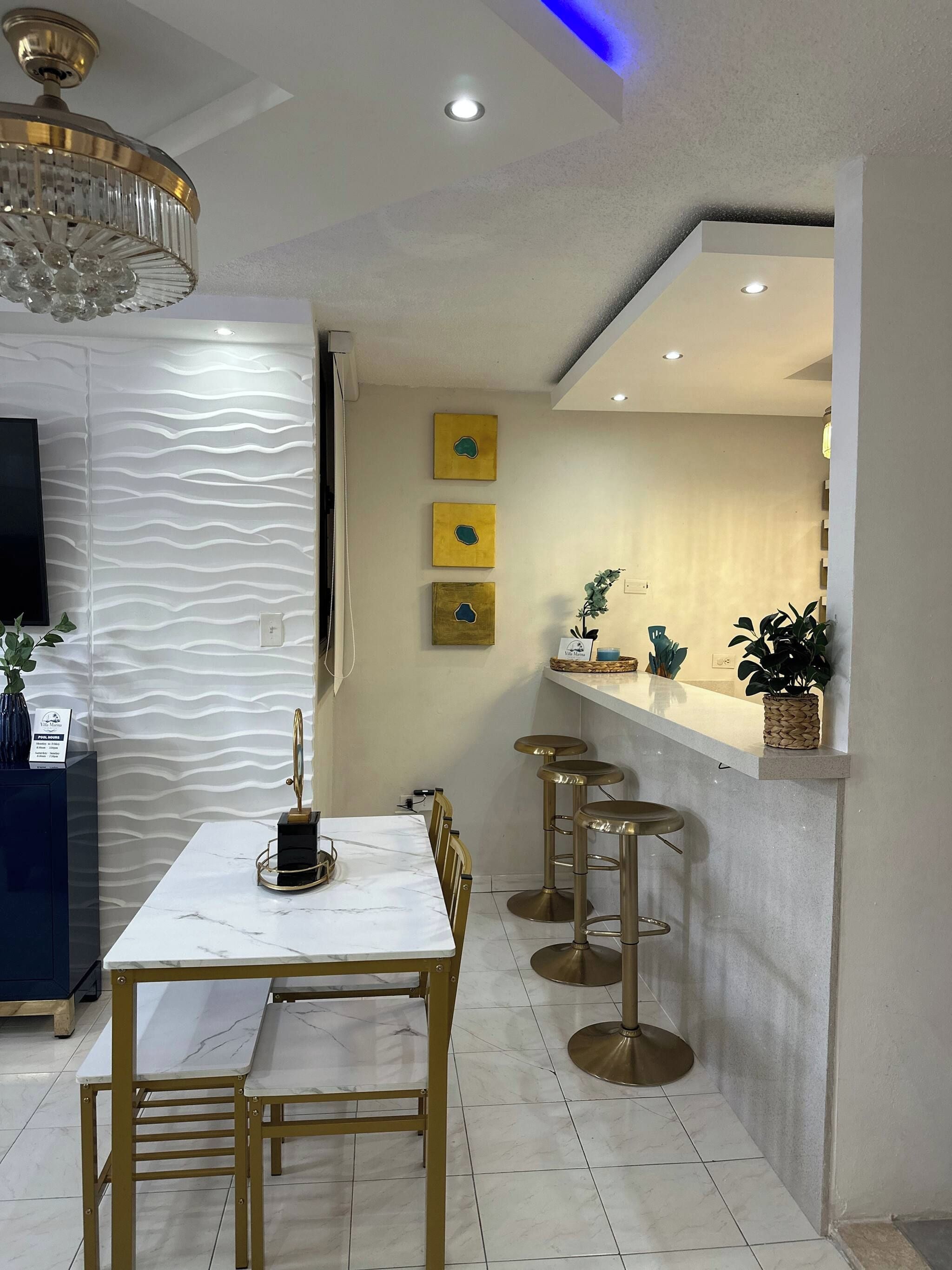 A modern dining area with a marble table, gold chairs, and a bar with stools.
