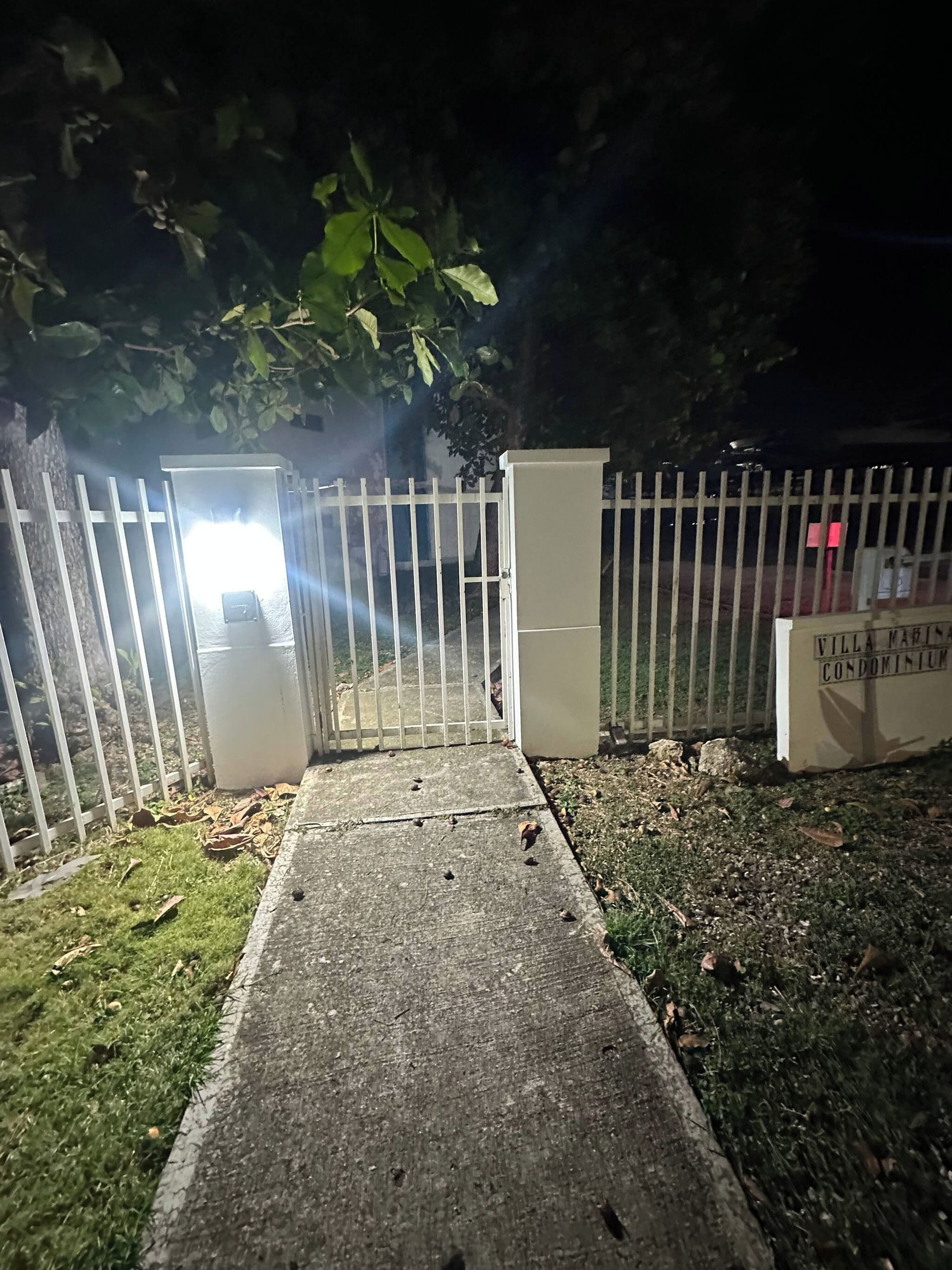 A gated entrance with a metal fence and a concrete pathway leading to a building.