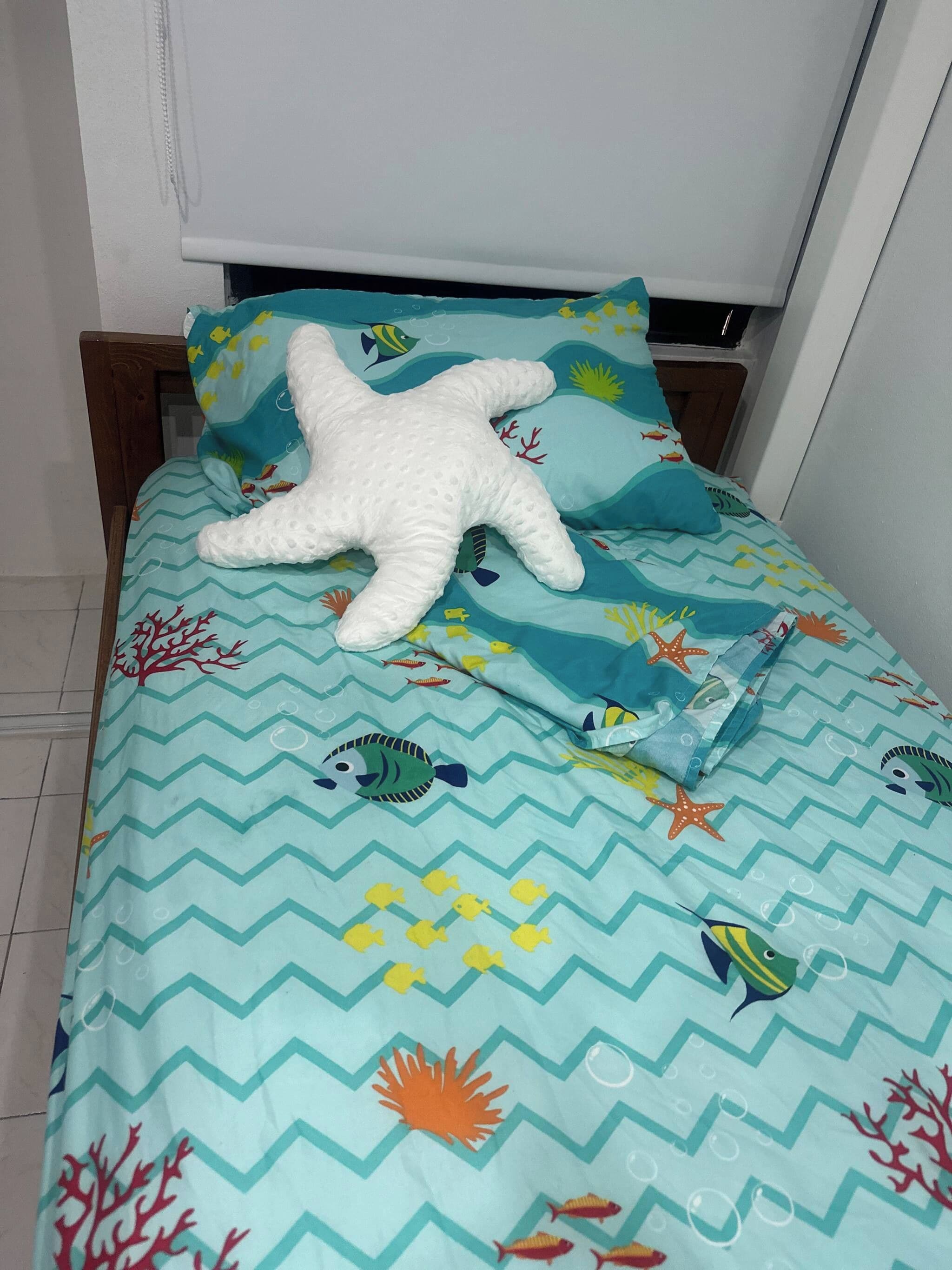 Una cama con un cojín con forma de estrella de mar y una colcha con motivos marinos.