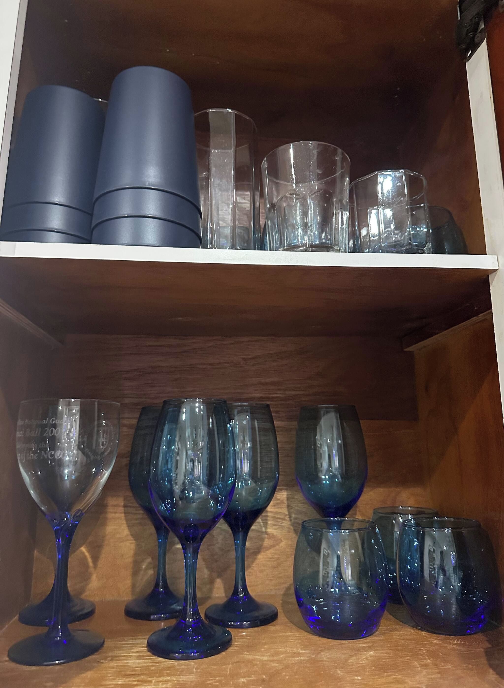 A shelf with various glassware including tumblers, wine glasses, and a set of blue tumblers.