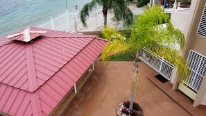 A balcony with a red roof, a palm tree, and a view of the beach. - Ventana Azul Direct Beach Access Condo (Cabo Rojo)