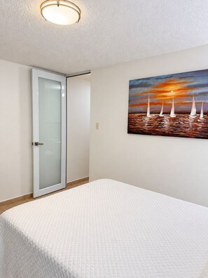 A bedroom with a bed, a painting of sailboats, a door, and a ceiling light. - Ventana Azul Direct Beach Access Condo (Cabo Rojo)