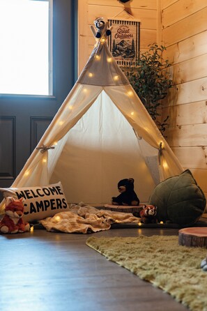 Um ambiente aconchegante com uma tenda tipi, um cartaz de boas-vindas, brinquedos macios e um quadro na parede.