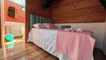 Ein Zimmer mit Holzboden, einem Bett, einem Fenster und einem durch eine geöffnete Tür sichtbaren Badezimmer.