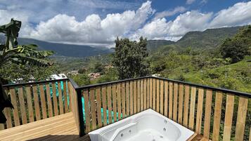 Eine Holzterrasse mit Whirlpool und Blick auf eine gebirgige Landschaft.