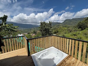 Eine Holzterrasse mit Whirlpool und Blick auf eine gebirgige Landschaft.