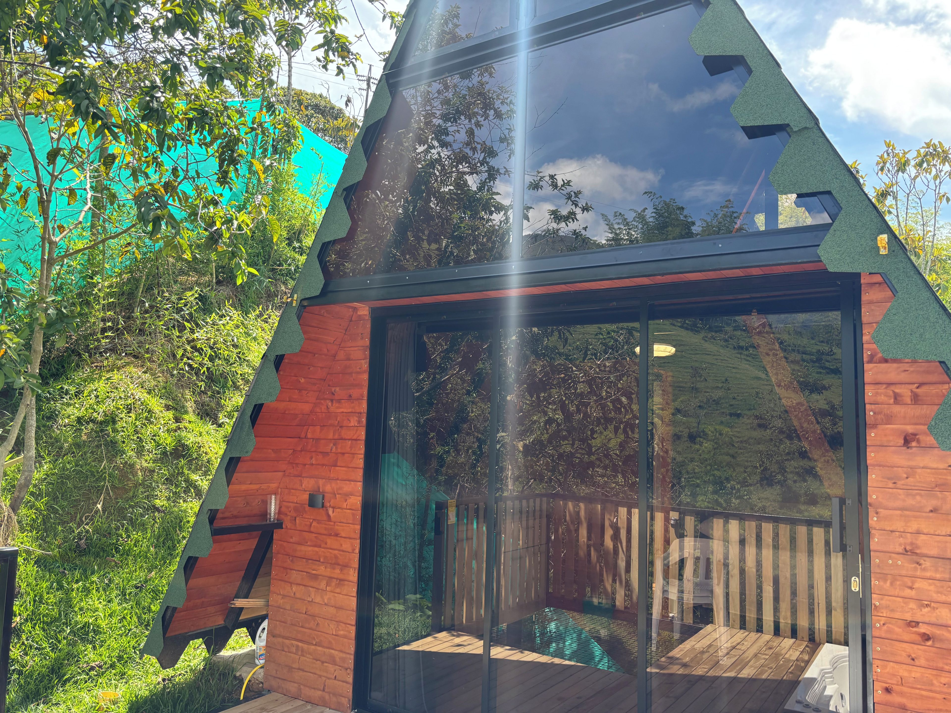 A modern wooden structure with a glass entrance, surrounded by greenery.