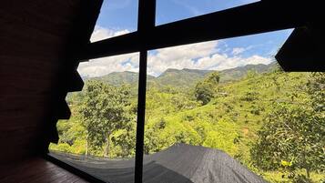 Ein Zimmer mit einem großen Fenster mit Blick auf eine üppige grüne Landschaft und Berge in der Ferne.