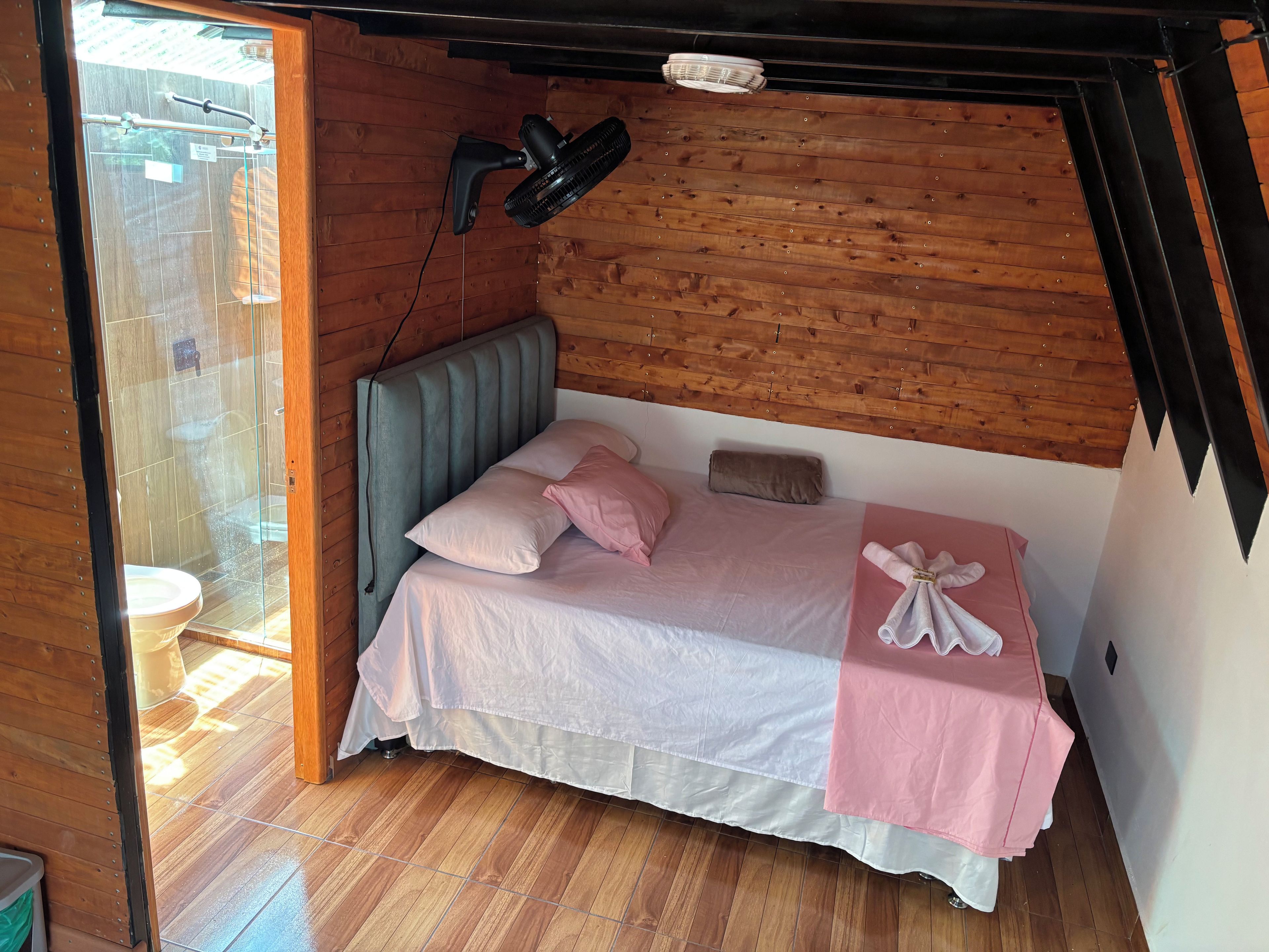 Ein Schlafzimmer mit Holzboden, einem Bett mit rosa Bettwäsche, einem Kopfteil und einem Handtuch auf dem Bett.