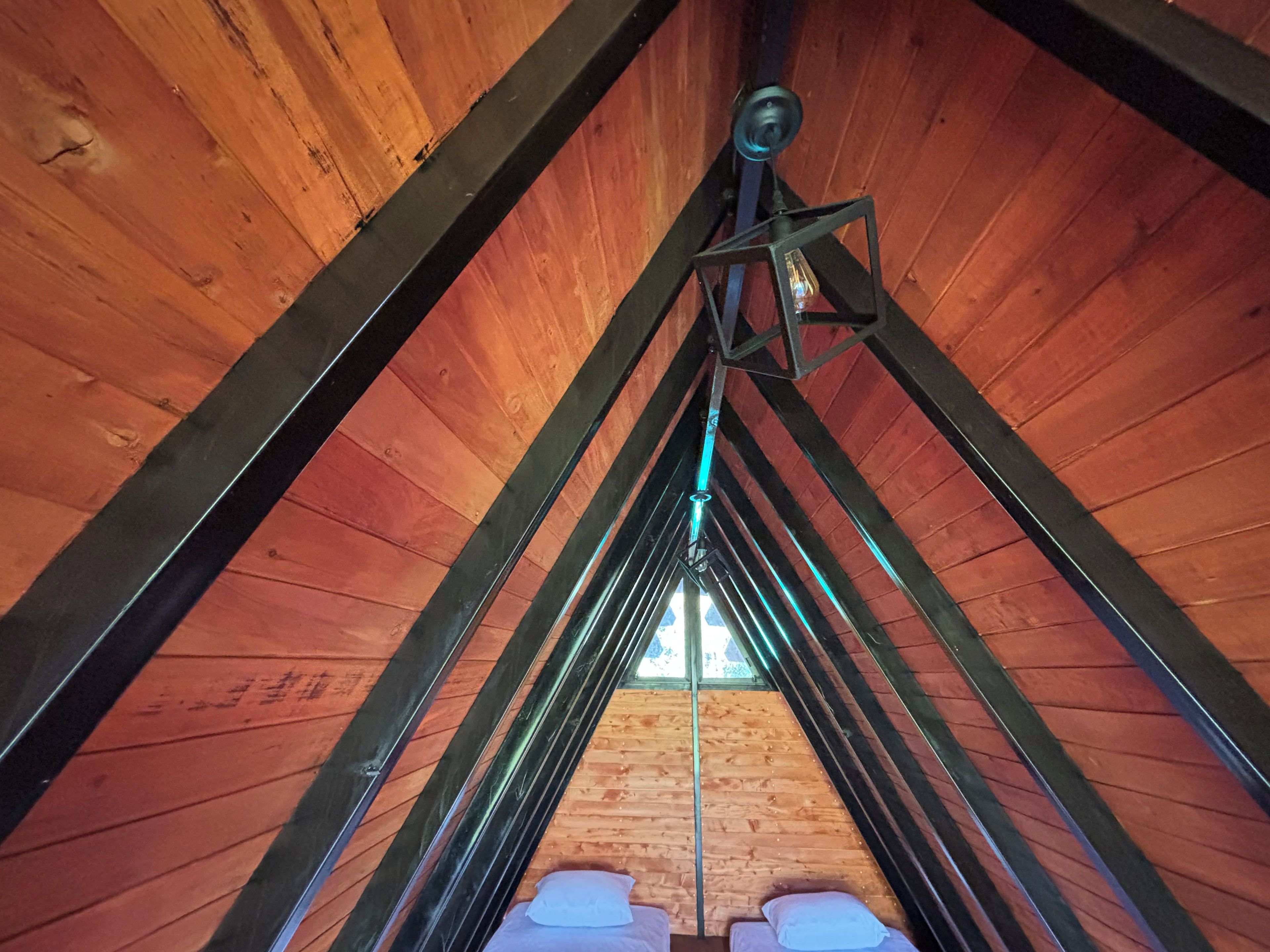 Une pièce mansardée en bois, avec un plafond en pente, des poutres apparentes et un luminaire suspendu.