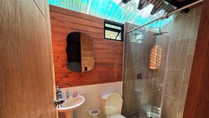 A compact bathroom with a wooden vanity, a sink, a toilet, and a glass-enclosed shower area. - Alegria Stay Glamping in Cocorná (Cocorná)