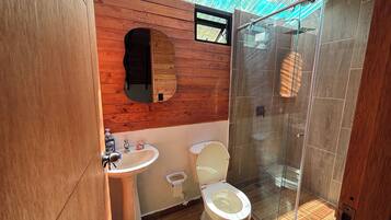 Ein kleines Badezimmer mit einem Holzbadezimmerhocker, einem Waschbecken, einer Toilette und einer Duschkabine.