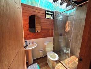 Ein kleines Badezimmer mit einem Holzbadezimmerhocker, einem Waschbecken, einer Toilette und einer Duschkabine.