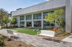 Ein modernes Gebäude mit Glasfassade, Außenbereich mit Sitzgelegenheiten und einem gepflegten Rasen.