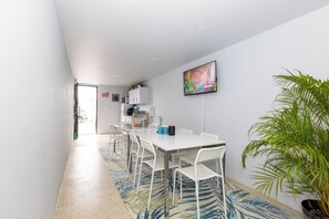 A modern dining area with a white table and chairs, a television mounted on the wall, and a potted plant. - Serena Villa (Carolina)