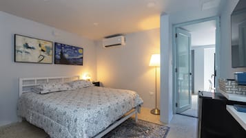 Un dormitorio con cama, lámparas de noche, aire acondicionado instalado en la pared y una puerta que da a otra habitación.