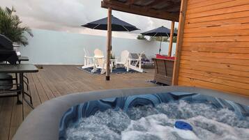An outdoor hot tub area with wooden deck flooring, lounge chairs, and umbrellas.
