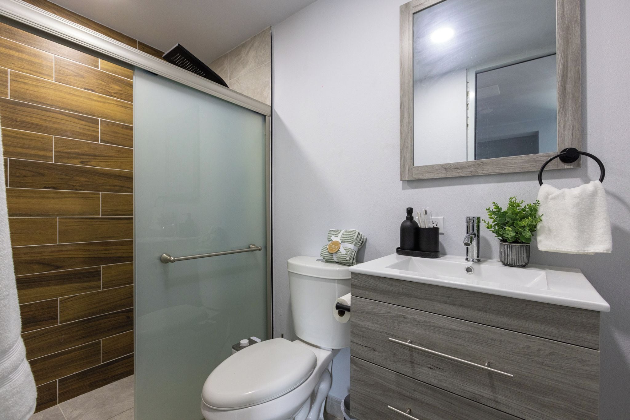 Un baño con inodoro, cabina de ducha, lavamanos con espejo y un perchero para toallas.