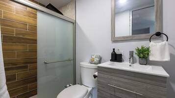 Un baño con inodoro, cabina de ducha, lavamanos con espejo y un perchero para toallas.