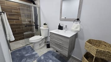 Une salle de bain moderne avec une douche à parois de verre, des toilettes, un meuble-lavabo avec un miroir et deux tapis bleus.