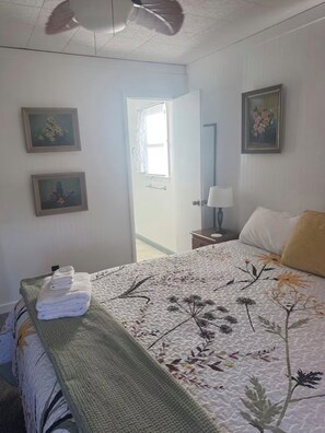 A bedroom with a bed, a nightstand, a lamp, and two framed pictures on the wall. - JUST RIGHT OBX 3-bedroom house in Nags Head on the water with beautiful sunsets (Nags Head)