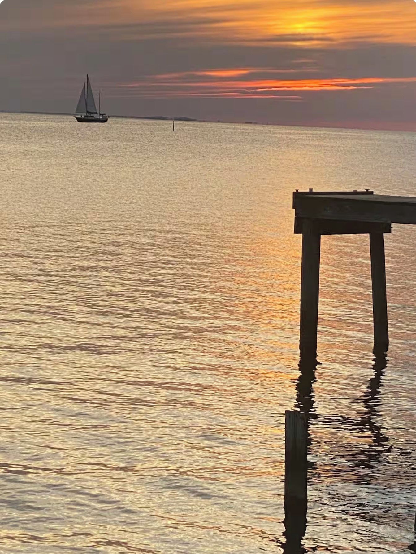 A calm body of water with a sailboat in the distance and a wooden pier extending into the water.