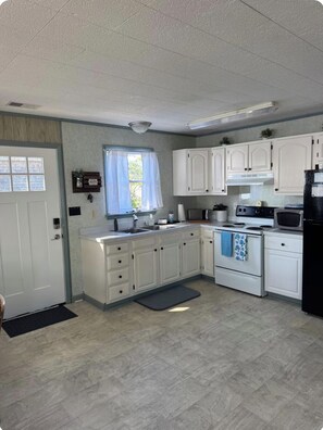 A kitchen with white cabinets, a microwave, stove, and a sink. - JUST RIGHT OBX 3-bedroom house in Nags Head on the water with beautiful sunsets (Nags Head)