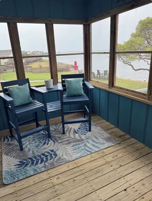 A room with a view of a body of water, two chairs with cushions, a small table, and a patterned rug on a wooden floor. - JUST RIGHT OBX 3-bedroom house in Nags Head on the water with beautiful sunsets (Nags Head)