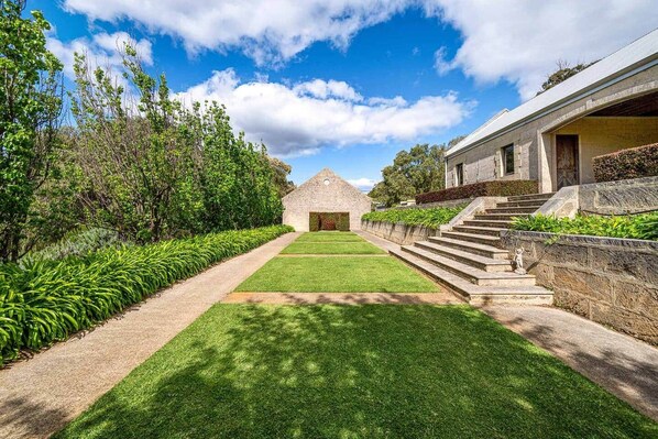 A stone building with a triangular roof, a paved pathway leading to it, and a well-maintained lawn.