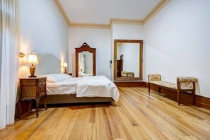 Camera d'albergo con un letto, due lampade da comodino, uno specchio grande, pavimento in legno e una panca.