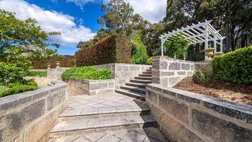 Un escalier en pierre mène à une pergola blanche située dans un jardin aménagé.
