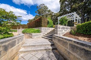 A stone staircase leading up to a white pergola in a landscaped garden.