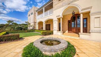 A large, classical building with a symmetrical facade, a central courtyard with a circular water feature, and a well-maintained garden.