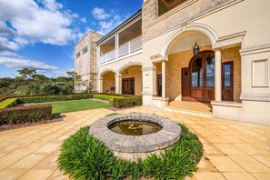 Un grande edificio classico con una facciata simmetrica, un cortile centrale con una fontana circolare e un giardino curato.