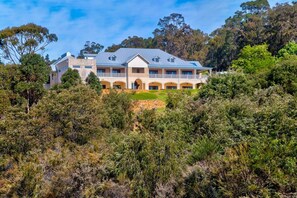 A large, two-story house with a balcony, surrounded by dense vegetation.