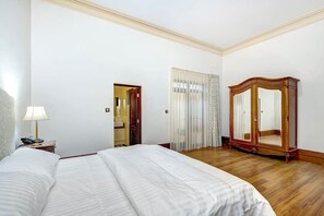 Una camera d'albergo con un letto grande, un armadio in legno, un comodino con una lampada e una porta che dà su un'altra stanza.