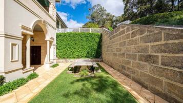 A courtyard with a stone wall, a grassy lawn, and a bench.