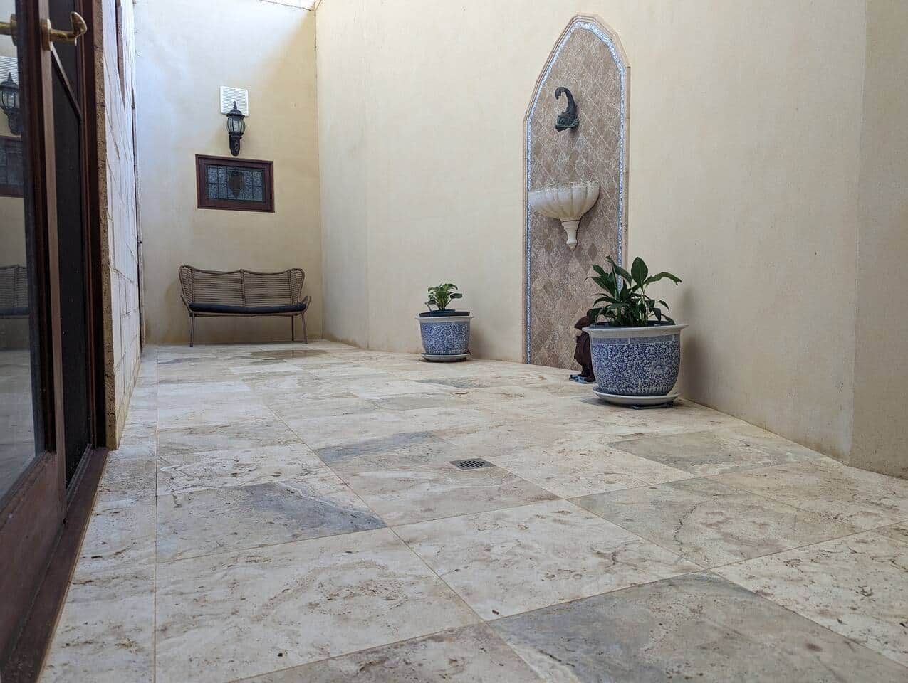 Un couloir avec un banc, deux plantes en pot, un luminaire fixé au mur et une porte dotée d’un panneau en verre.
