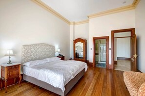 Una camera da letto con un letto grande, comodini in legno, uno specchio e una porta che dà su un'altra stanza.