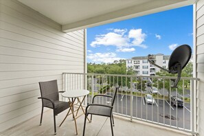 A balcony with two wicker chairs and a small round table, overlooking a parking lot and buildings. - 15 Min to Disney | Kissimmee 3BR/2BA | Sleeps 10 (Kissimmee)