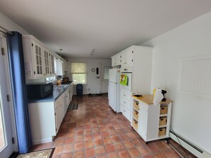 Una cocina con armarios blancos, encimera negra, suelo de baldosas, un refrigerador y un microondas.