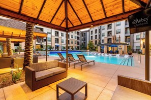 A poolside area with lounge chairs, a covered seating area, and a sign for 'the Abbey at Northpoint.' - Stunning Pool View 2 Bedroom Apartment (Spring)