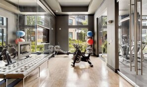 A gym with exercise equipment, a bench, and large windows offering a view of the outside. - Stunning Pool View 2 Bedroom Apartment (Spring)