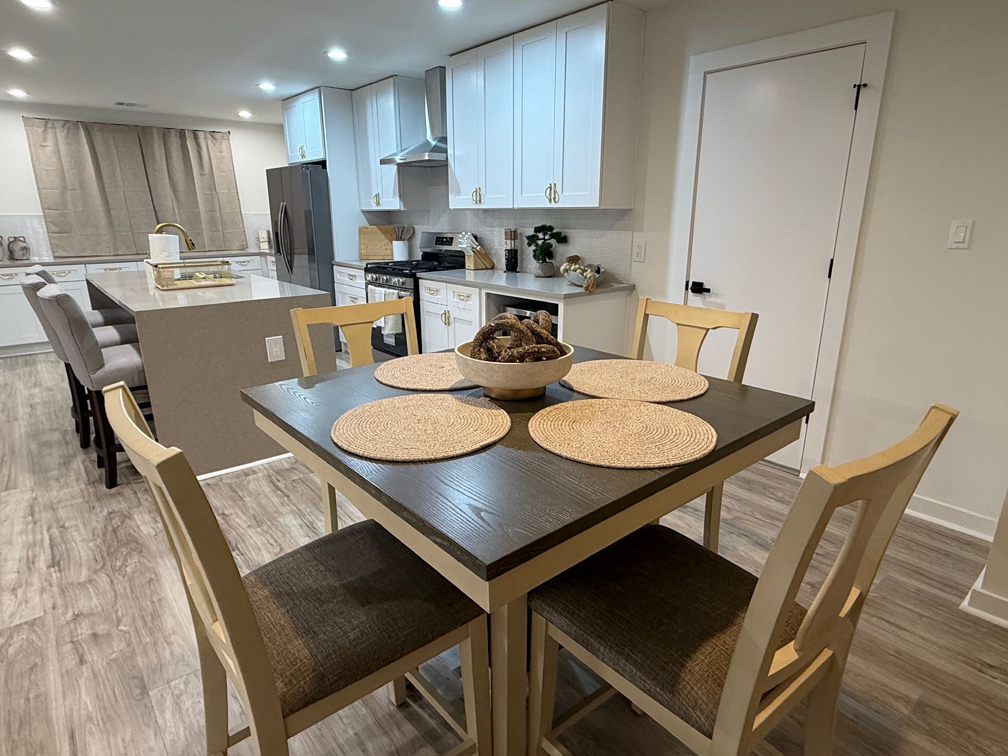 A modern kitchen with white cabinets, a central island, and a dining table with four chairs.