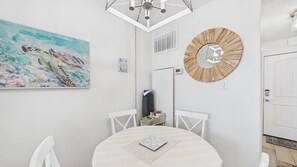A dining area with a round table, white chairs, a painting, a wall clock, and a door. - Gulfside Getaway 319-3rd Floor Beachfront-Sleeps 4 (Panama City)
