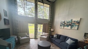 Una sala de estar con televisor, sofás, sillones, una mesa de centro y obras de arte en las paredes.